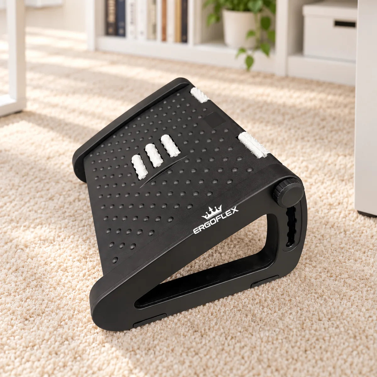 ErgoFlex black adjustable footrest with white crown logo in a home office on a neutral carpet