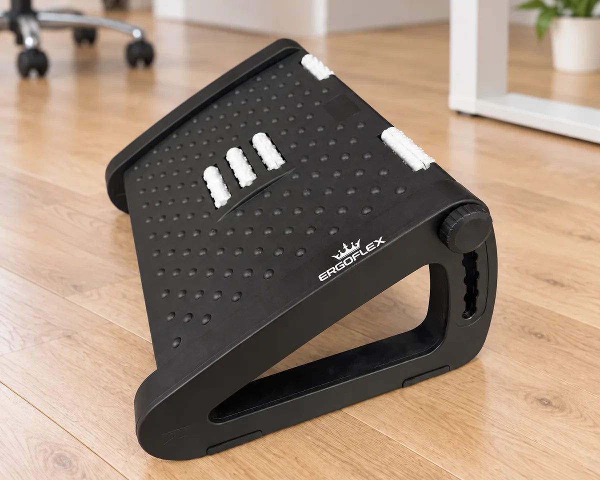 ErgoFlex black adjustable footrest with white crown logo beside an office desk on a wood floor
